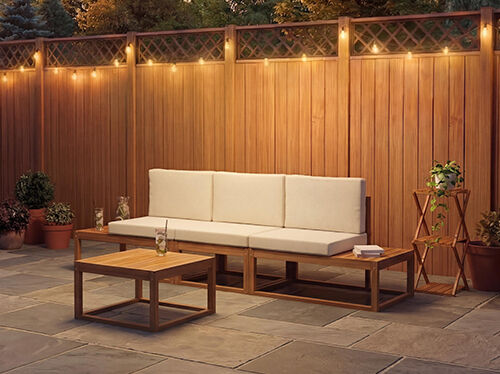 Canap&eacute; modulaire d'ext&eacute;rieur trois places avec des coussins cr&egrave;me et une table basse assortie, sur une terrasse en pierre face &agrave; un mur en bois chaleureux