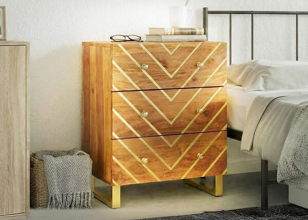 Table de chevet en bois &agrave; trois tiroirs avec motif g&eacute;om&eacute;trique dor&eacute;, plac&eacute;e &agrave; c&ocirc;t&eacute; d&rsquo;un lit dans une chambre lumineuse.