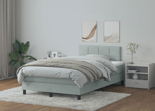 Lit &agrave; sommier tapiss&eacute; gris clair avec t&ecirc;te de lit &agrave; panneaux, literie blanche, table de chevet et coiffeuse en bois clair dans une chambre &agrave; coucher styl&eacute;e.