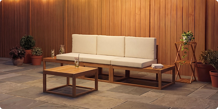 Canapé modulaire d'extérieur trois places avec des coussins crème et une table basse assortie, sur une terrasse en pierre face à un mur en bois chaleureux